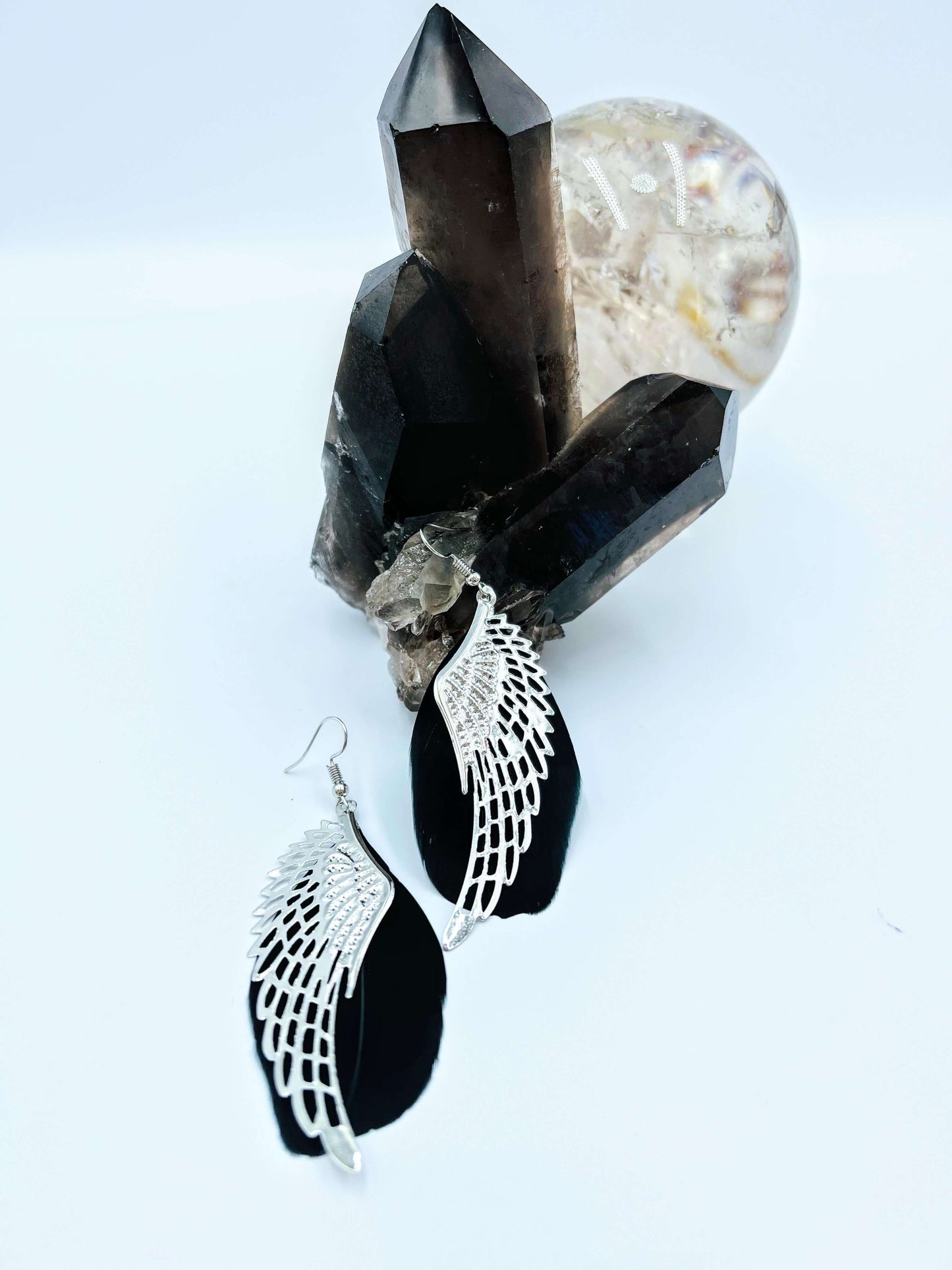 black feather angel wing earrings with metal feather overlay sitting on a smoky quartz crystal cluster.