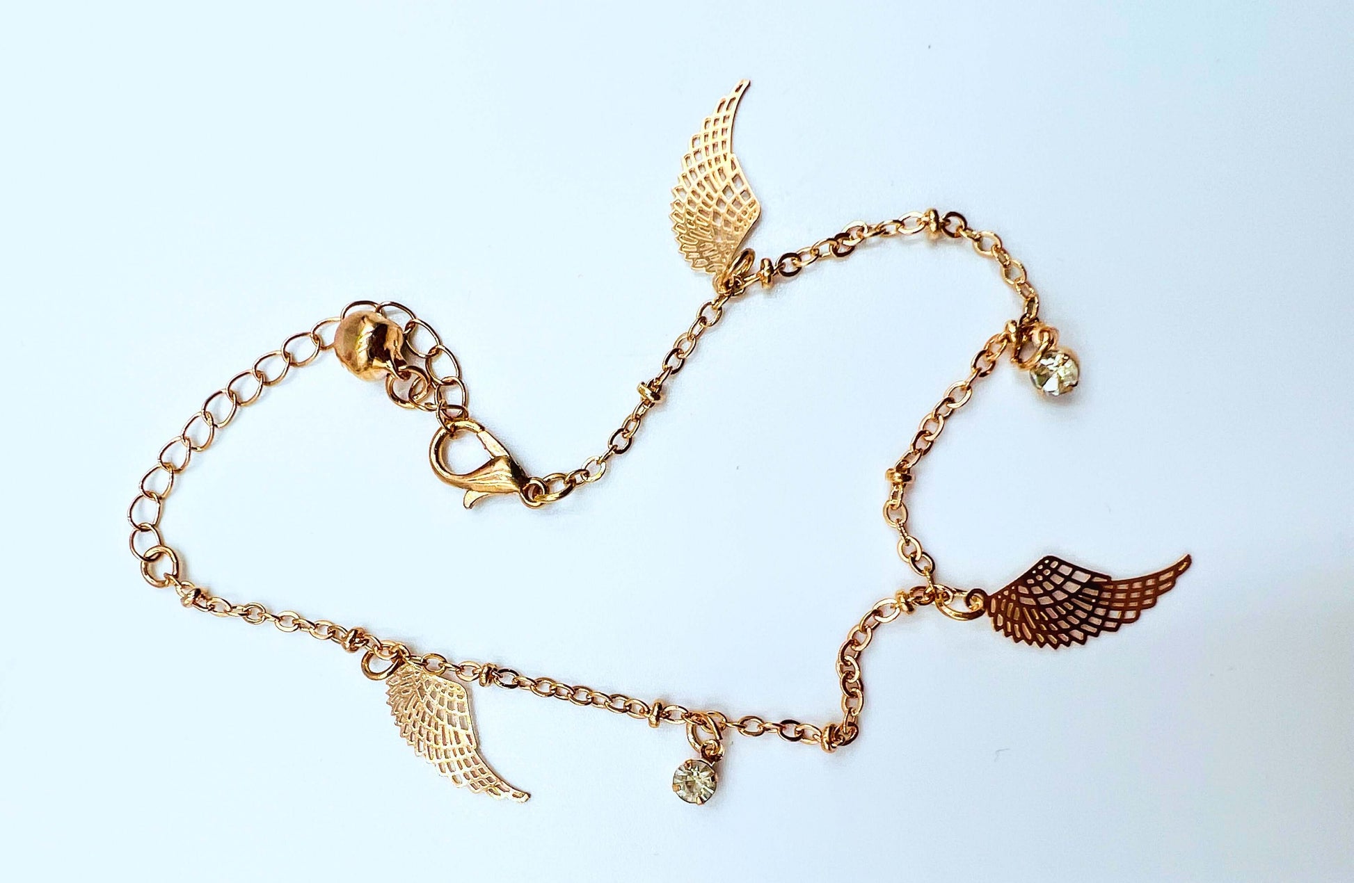 Ankle bracelet gold colour sitting on white surface.