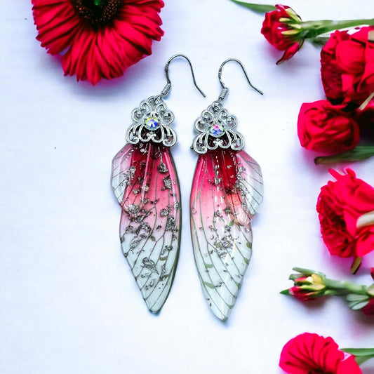 Fairy wing earrings with petals scattered on a white surface.