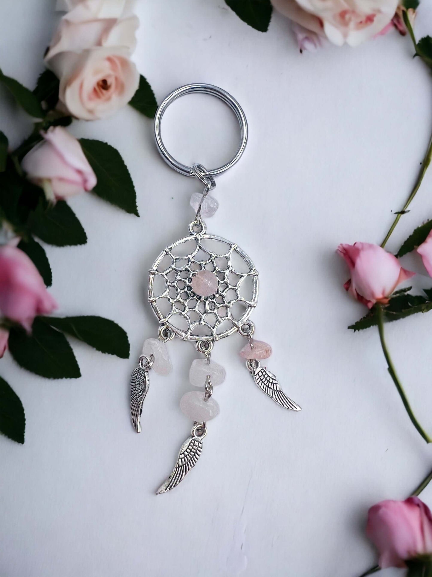 Dream catcher key ring with crystal chips on white surface surrounded with petals.