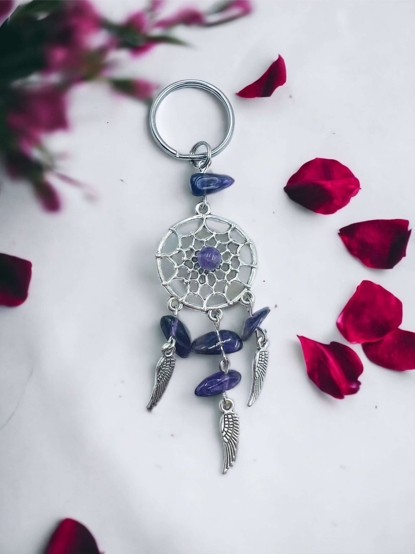 Dream catcher key ring with crystal chips on white surface surrounded with petals.