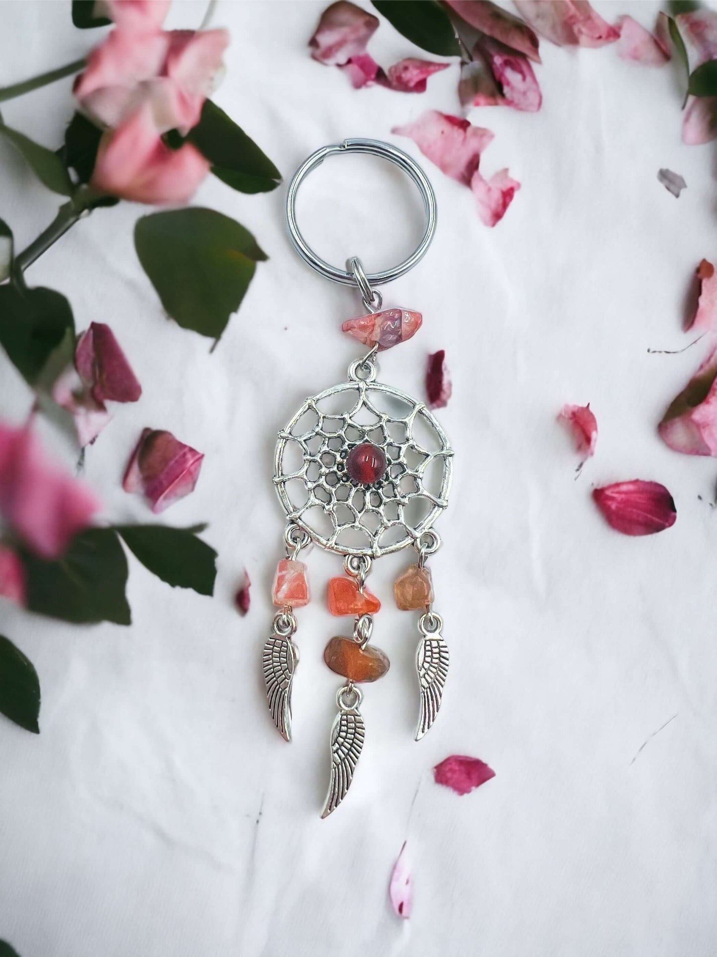 Dream catcher key ring with crystal chips on white surface surrounded with petals.