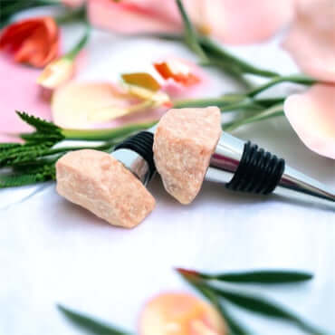 Moon stone wine bottle stoppers on white surface with petals 