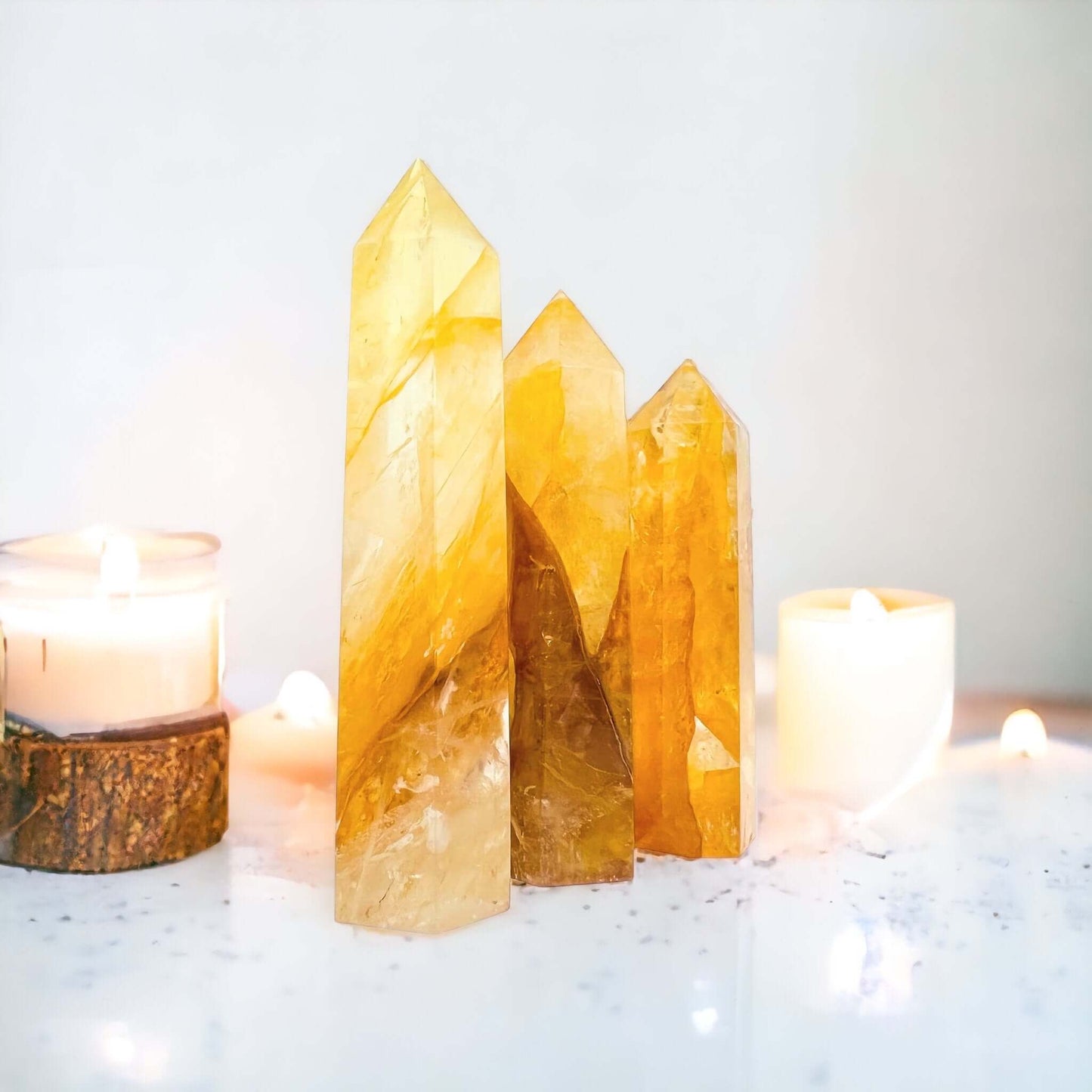 Golden healer quartz points on white surface with candles in background. 