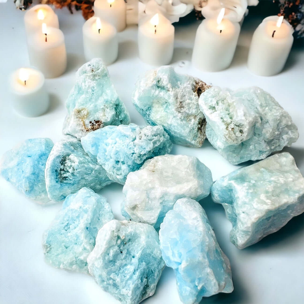 Several pieces of blue aragonite on white surface with candles in background 