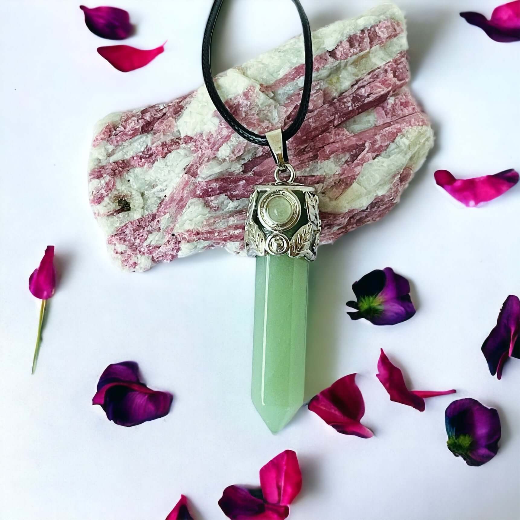 Green aventurine pendant on white surface with petals