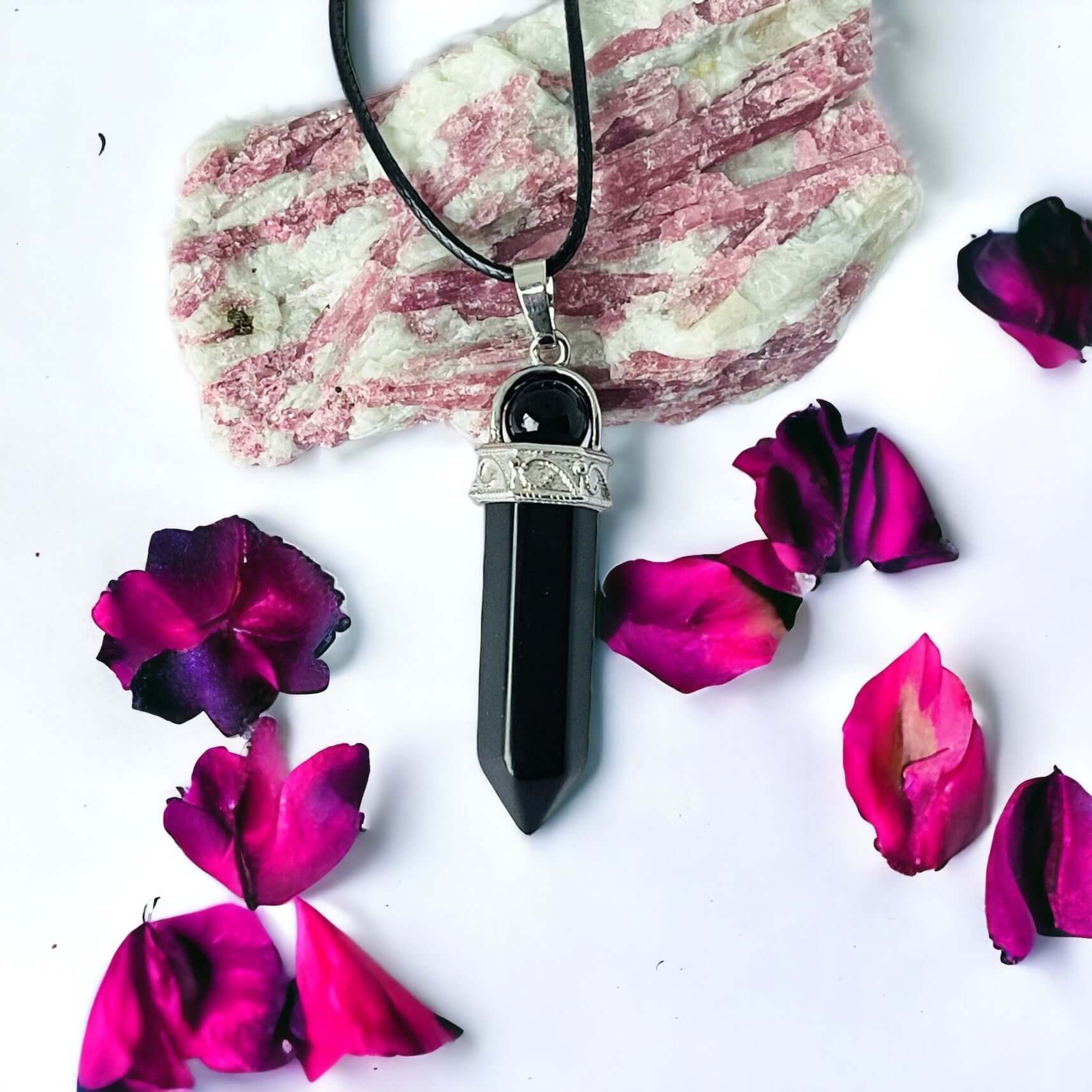 Black obsidian pendant on white surface with petals.