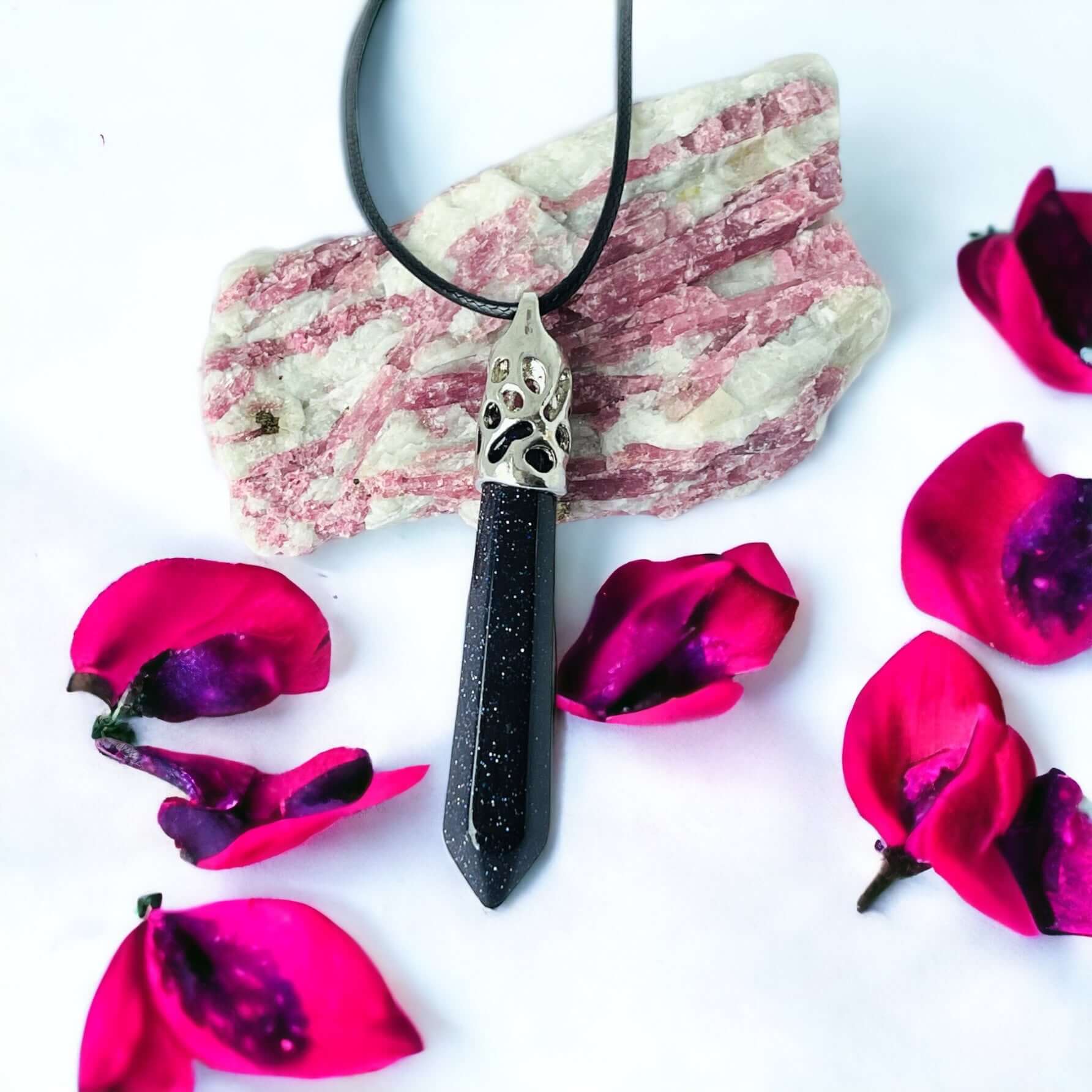 Black obsidian cats eye Long crystal pendant on white background with petals.