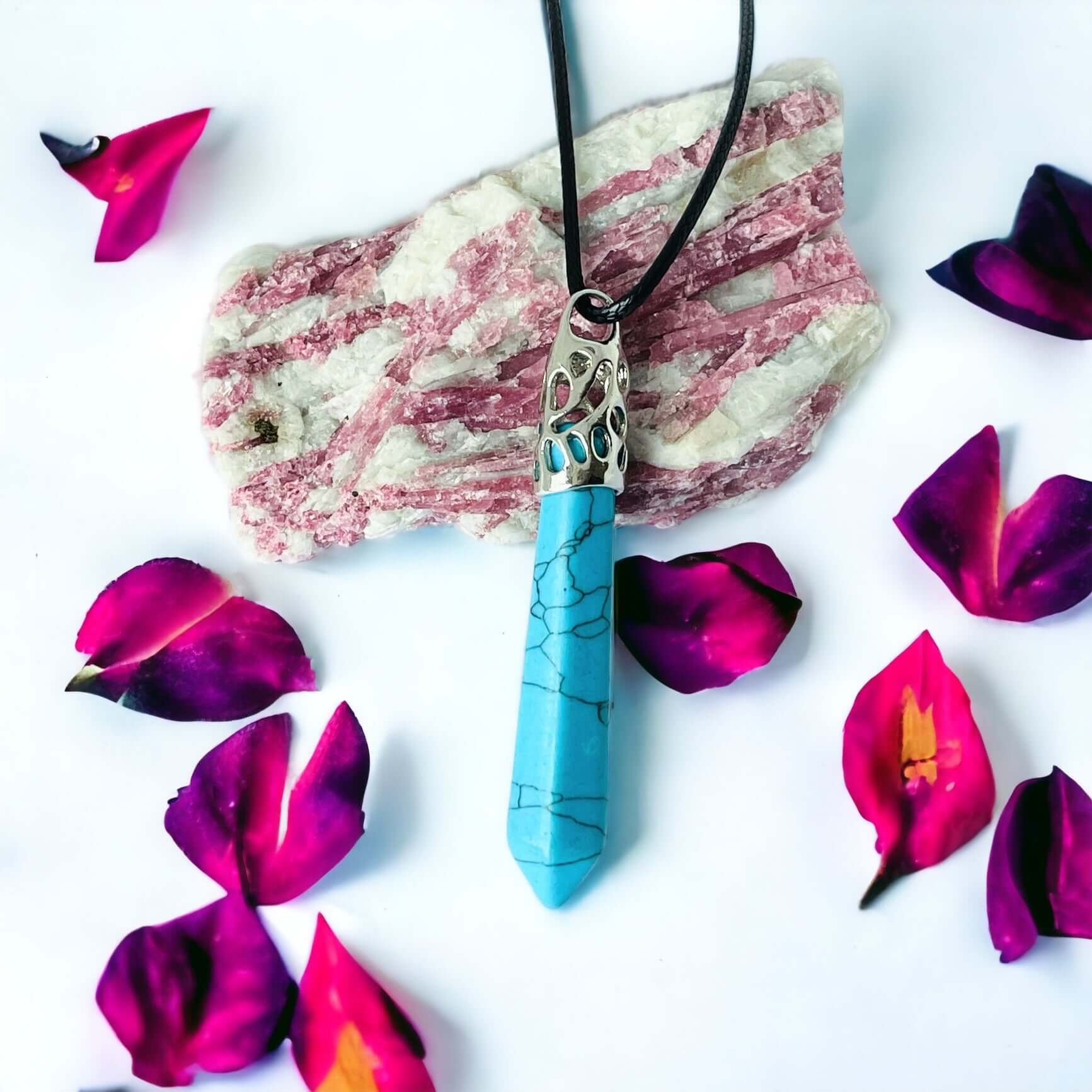 Blue howlite Long crystal pendant on white background with petals.