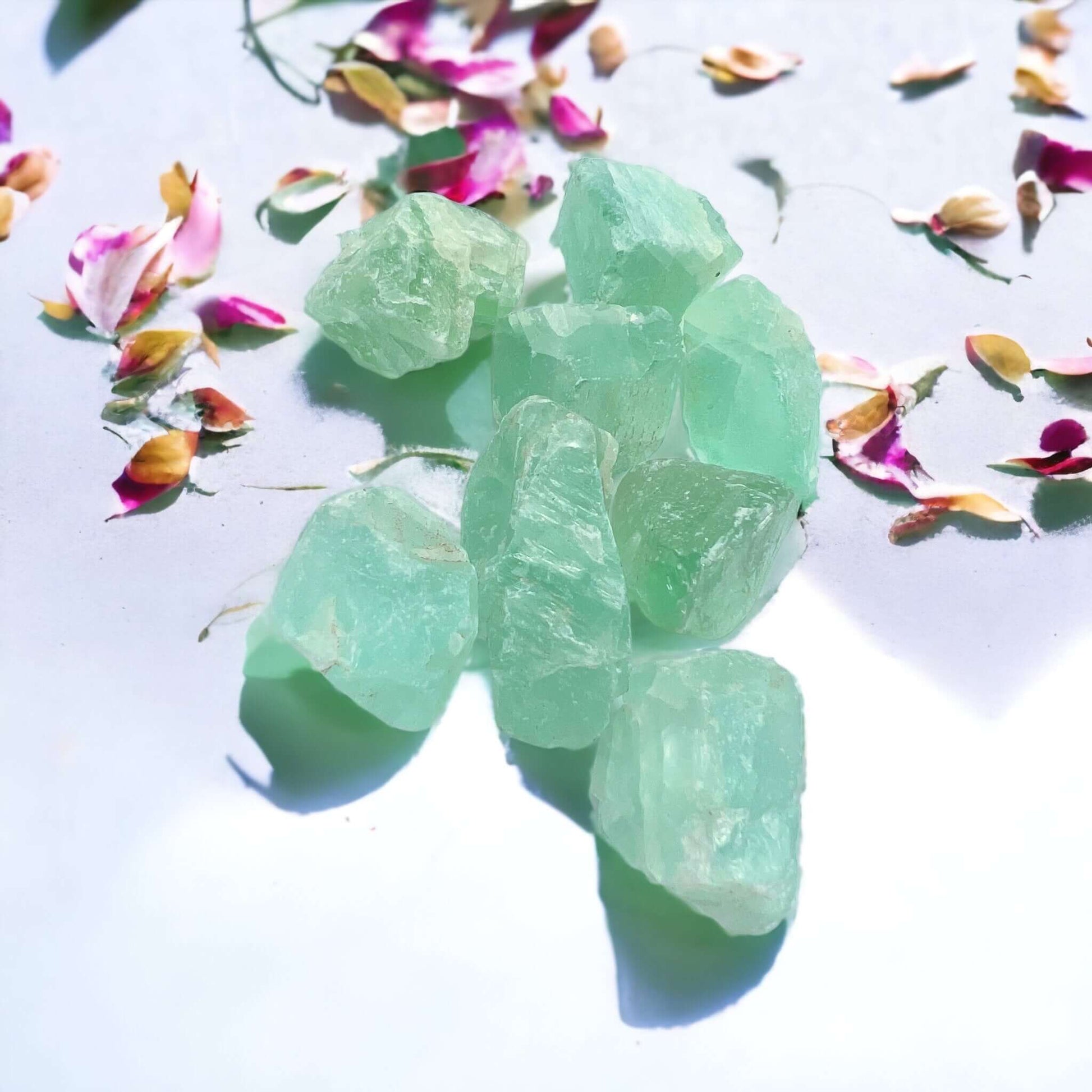 Rough green fluorite stones on white surface with petals scattered