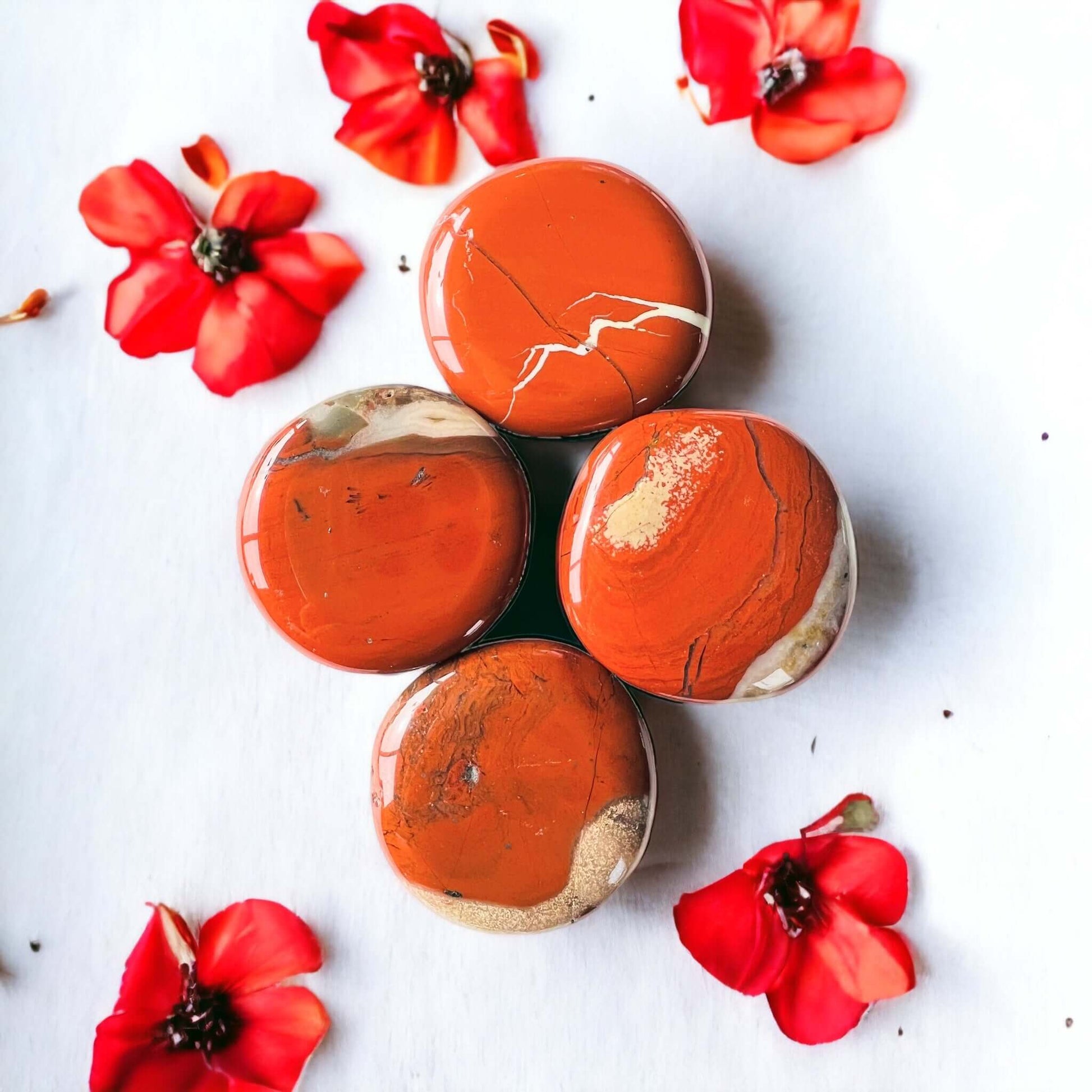 Red Jasper crystal pop sockets on white surface with scattered petals.