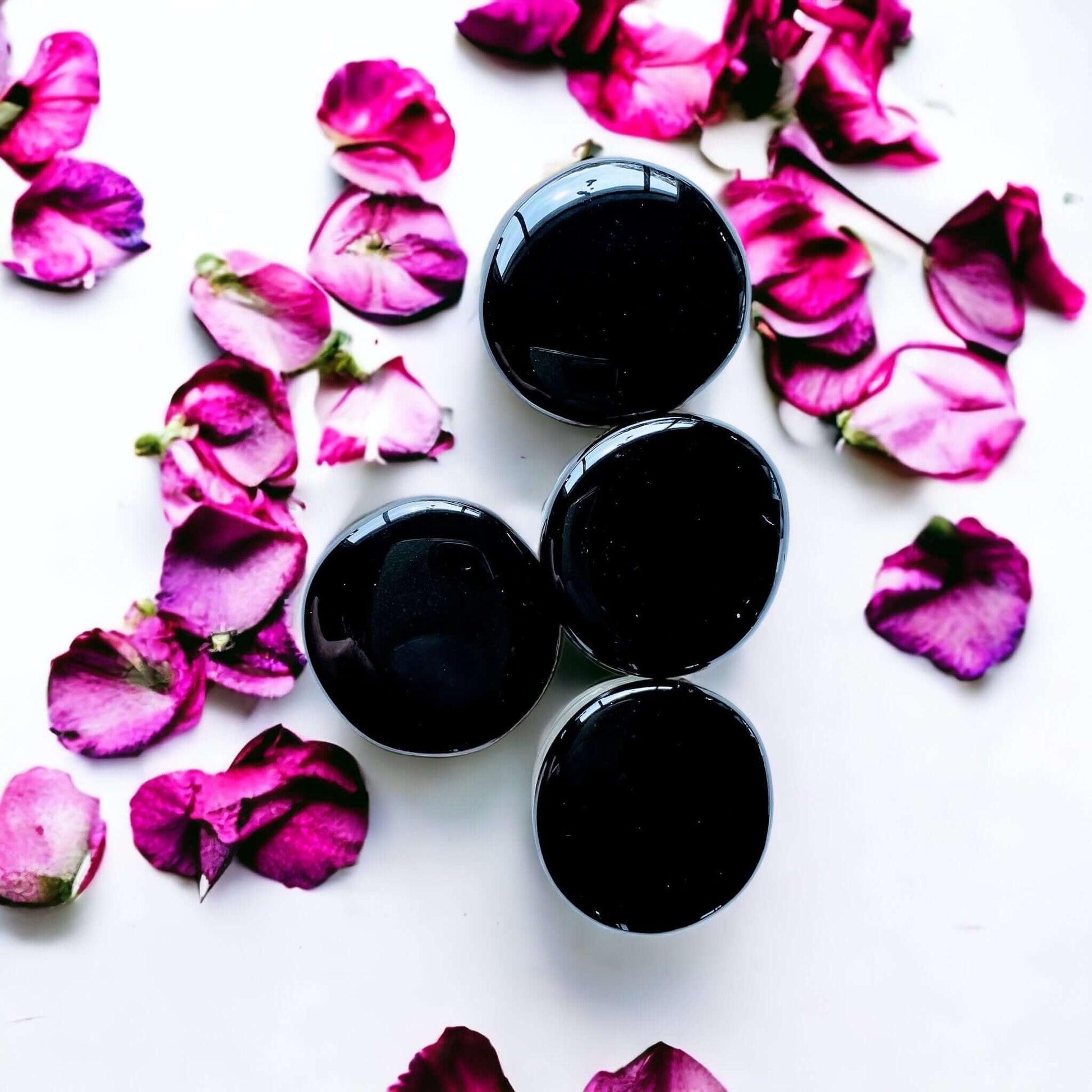 Black obsidian crystal pop sockets on white surface with scattered petals. 