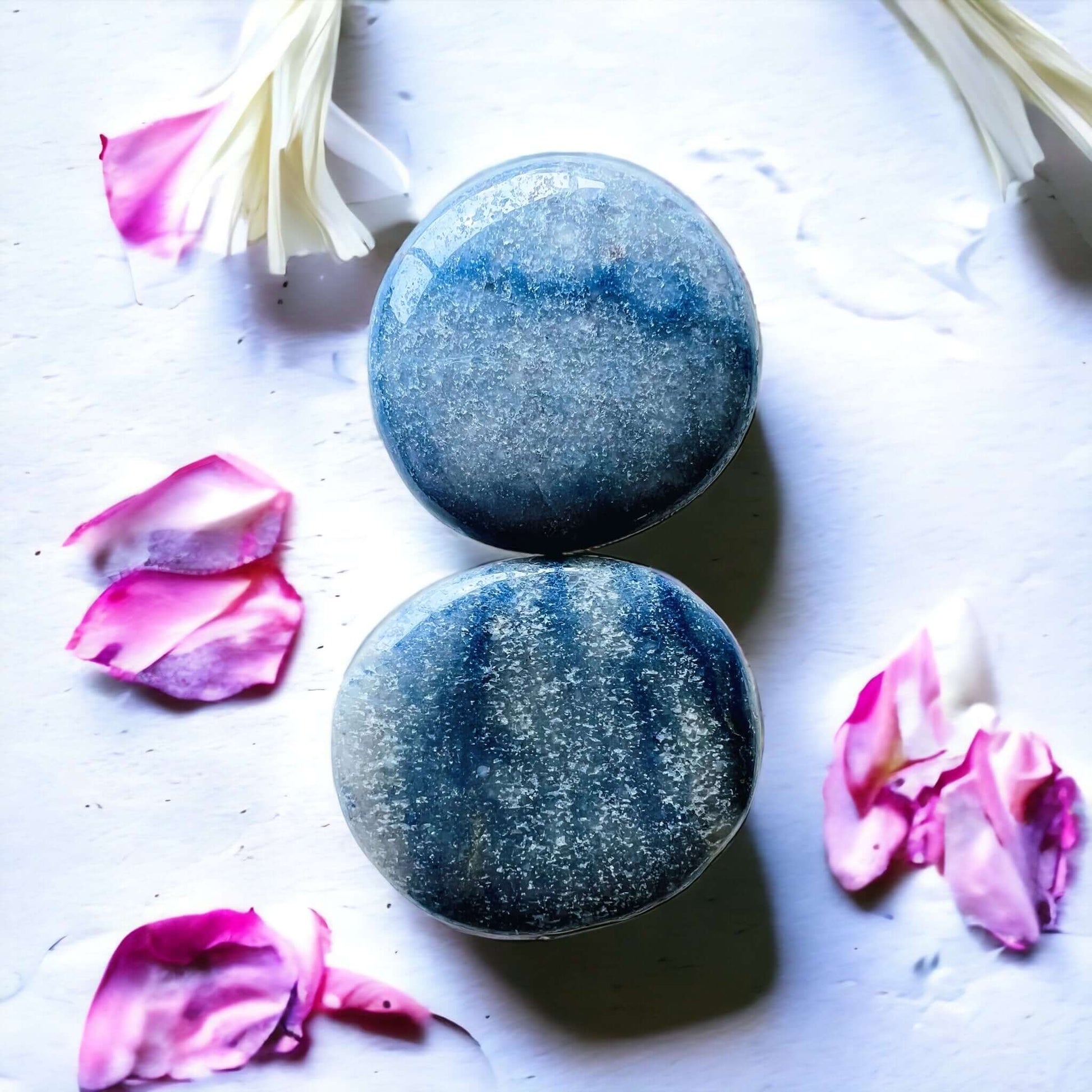 Blue aventurine crystal pop sockets on white surface with scattered petals.