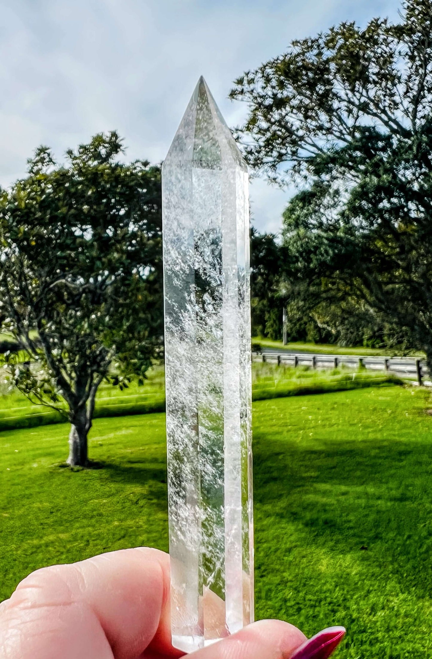 Clear quartz polished point held in hand with farm land in background.