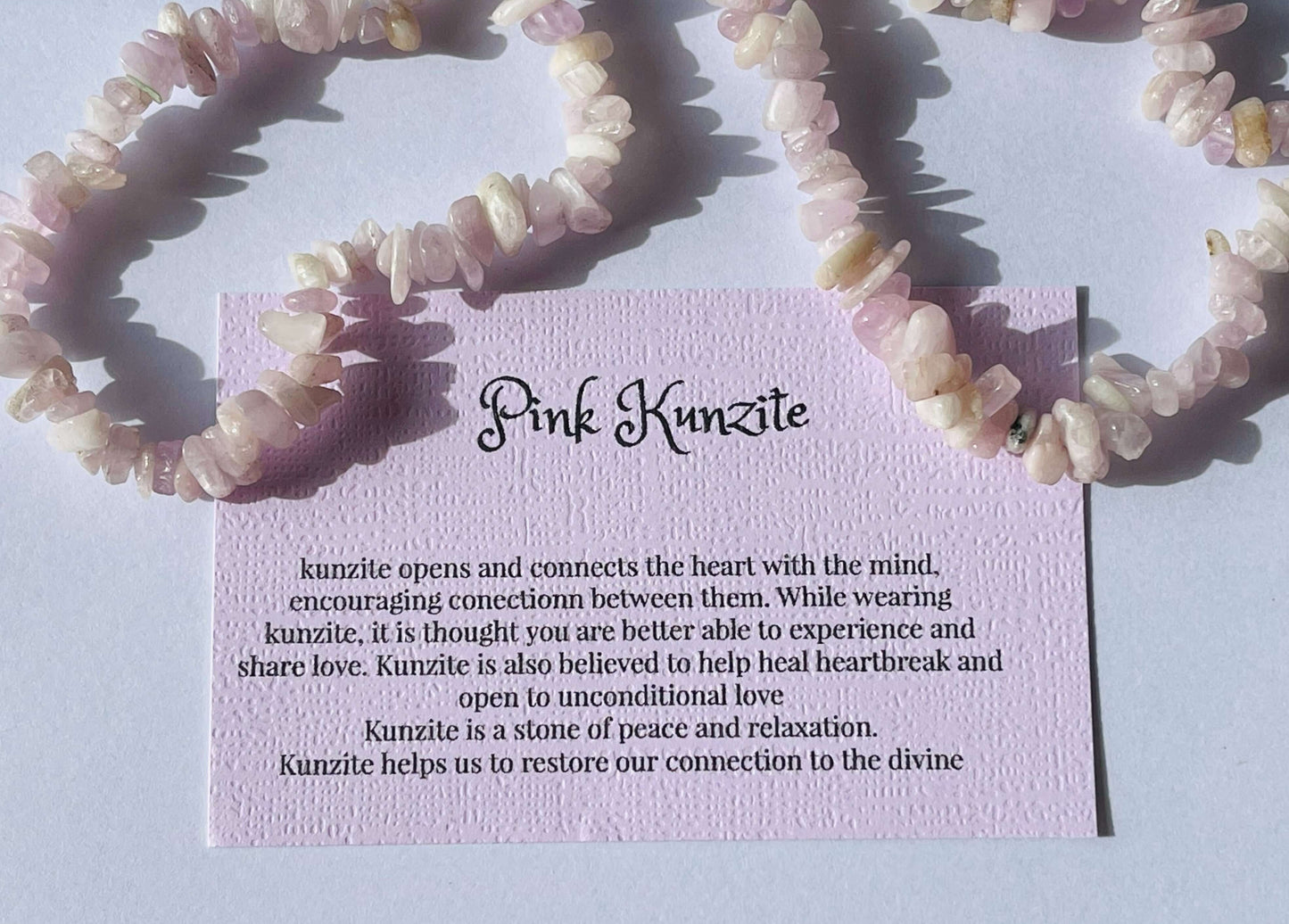 Pink kunzite crystal chip bracelet with information card on white background