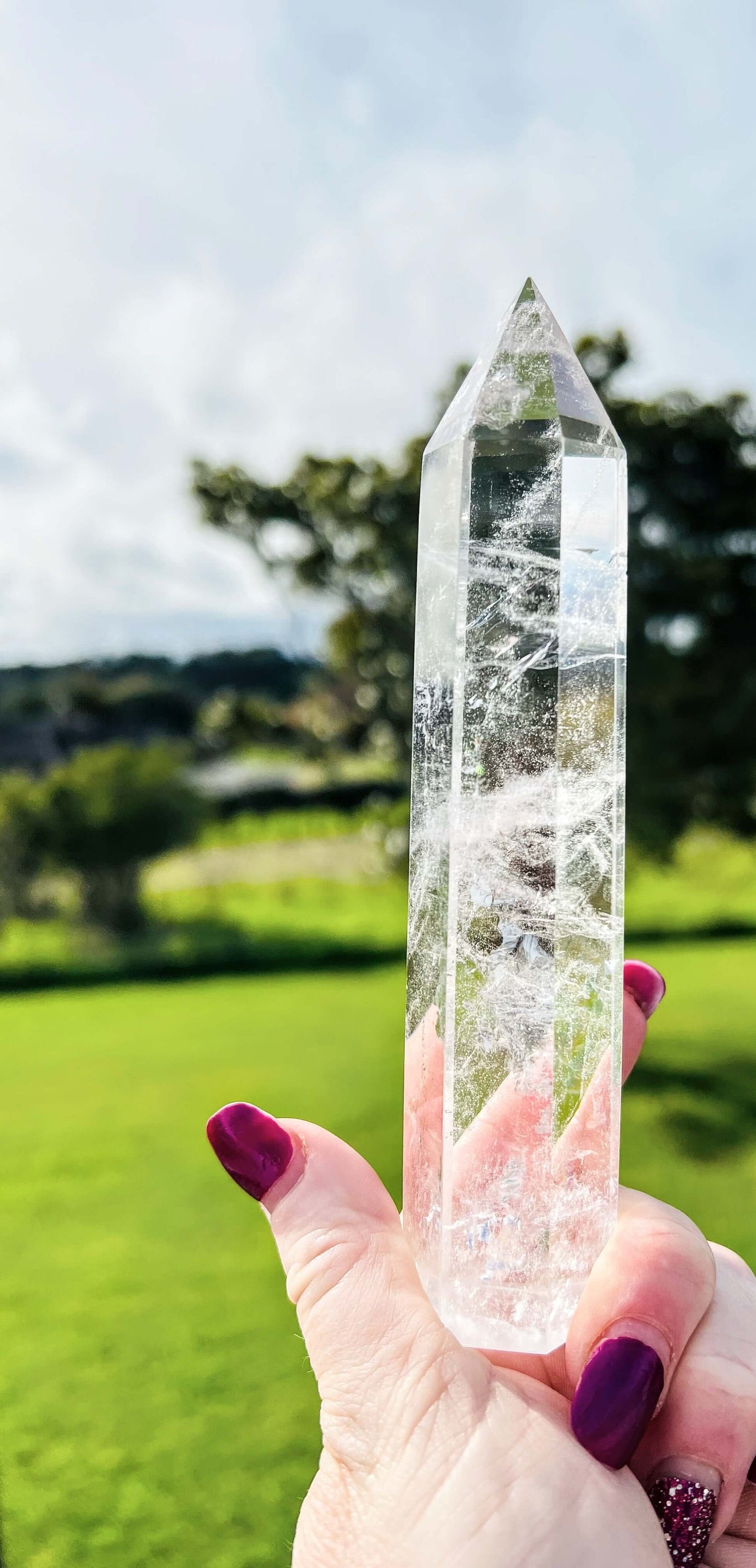 Clear quartz polished point held in hand with farm land in background.