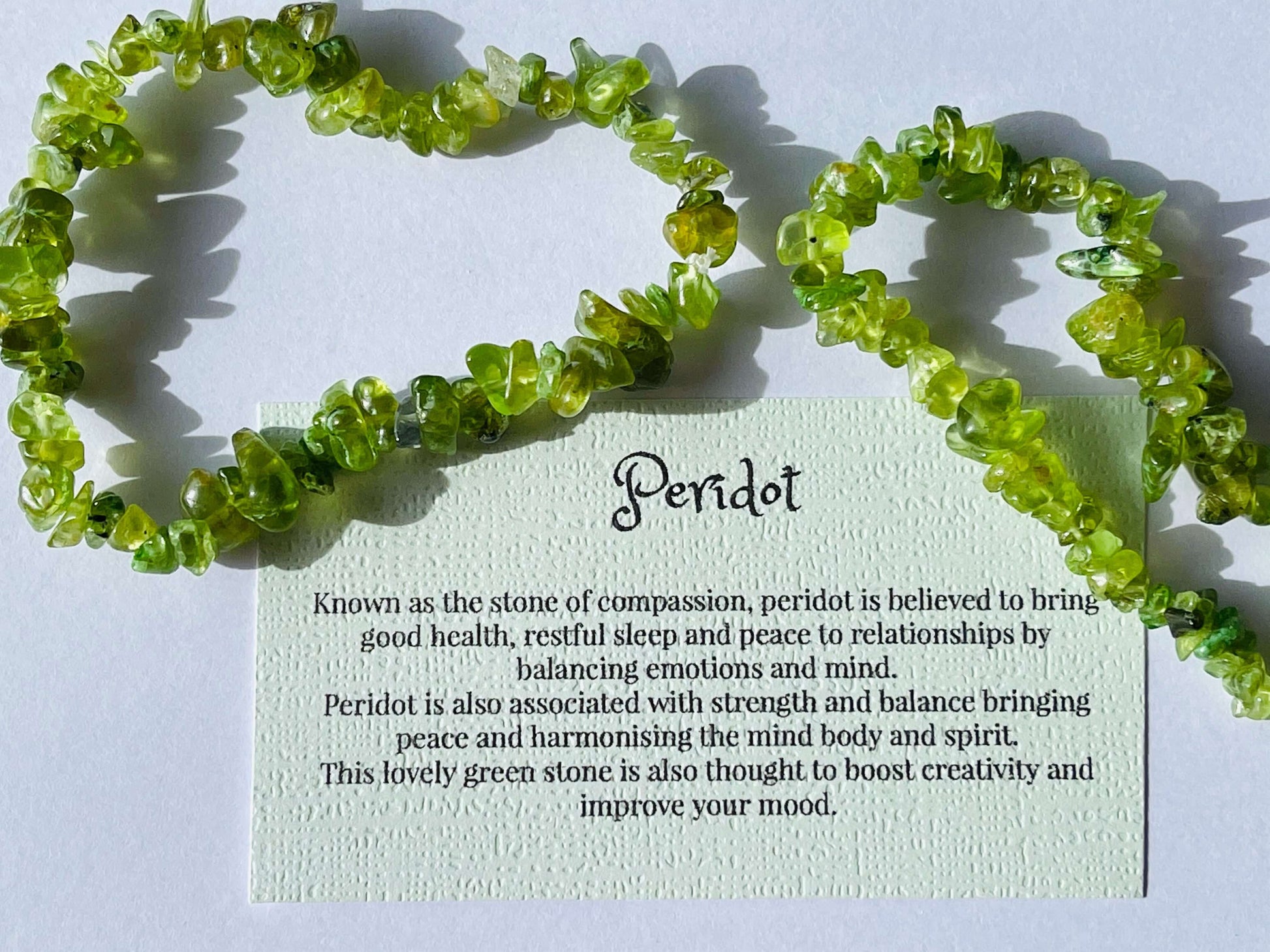 Peridot crystal chip bracelet with information card on white background