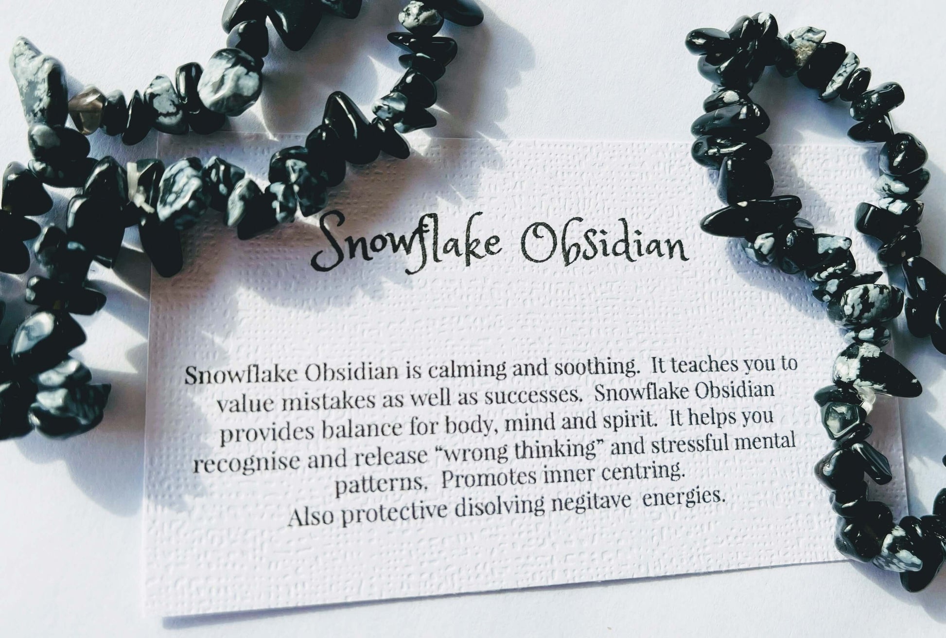 Snow flake obsidian crystal chip bracelet with information card on white background