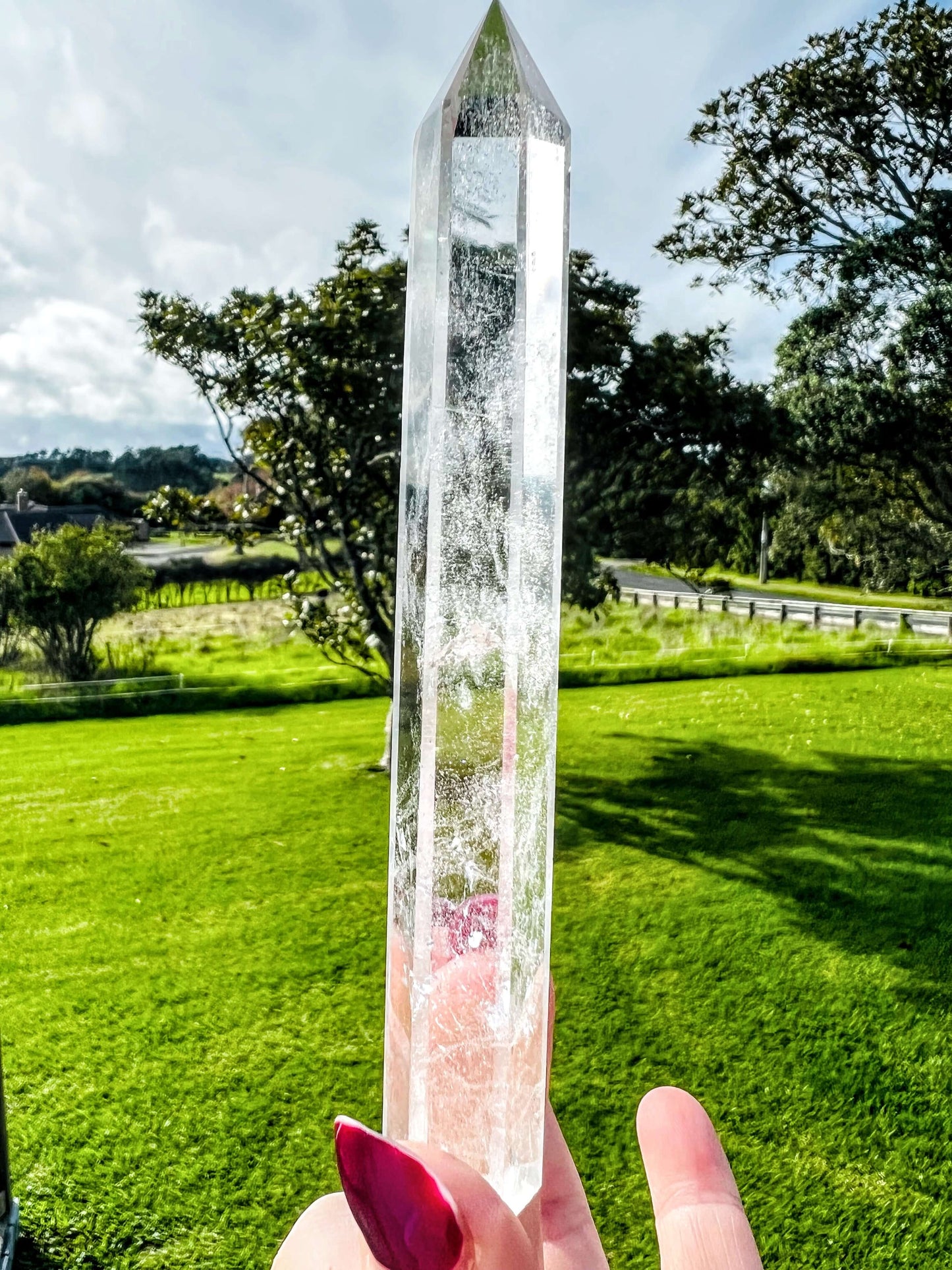 Clear quartz polished point held in hand with farm land in background.