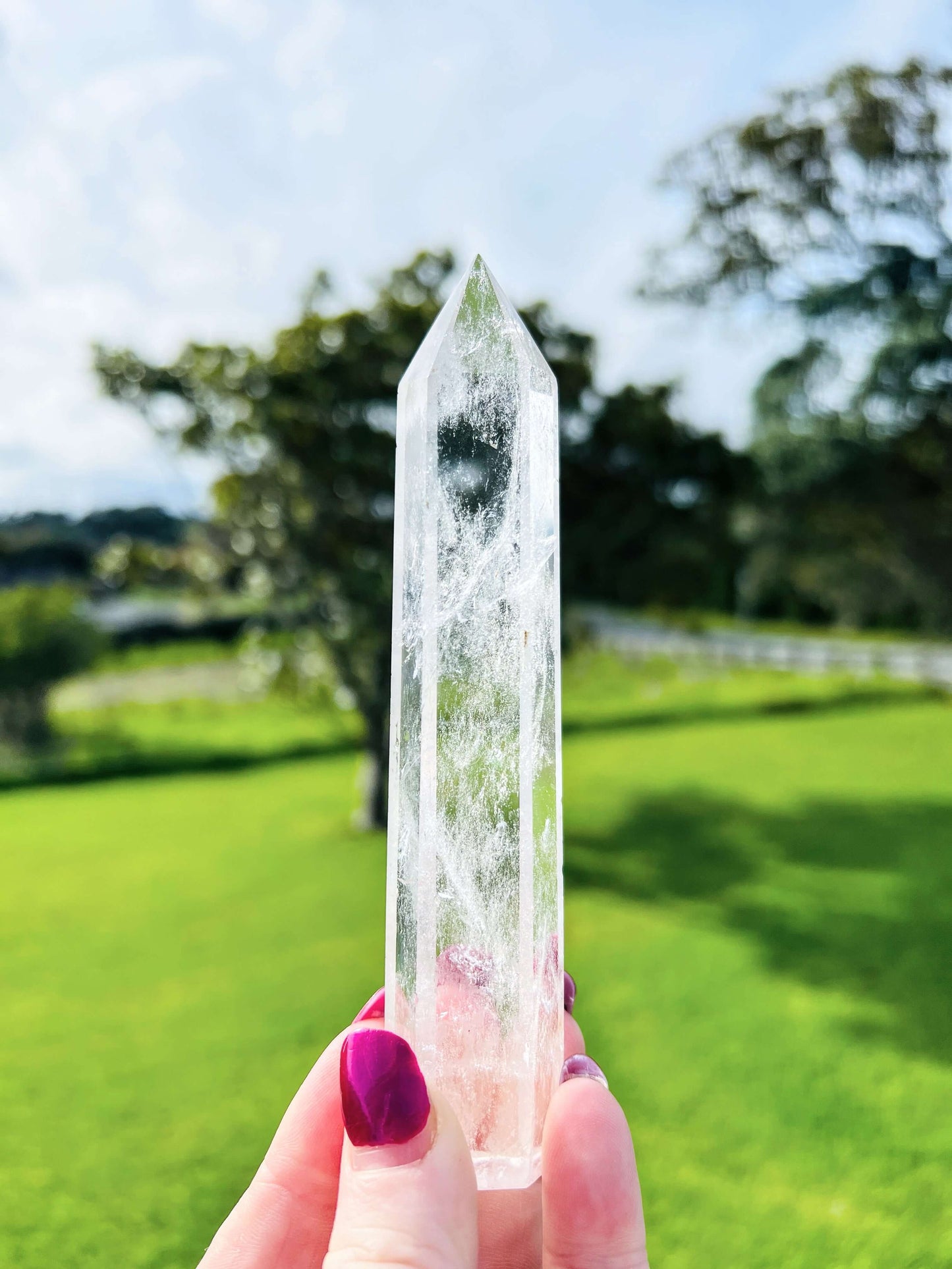 Clear quartz polished point held in hand with farm land in background.