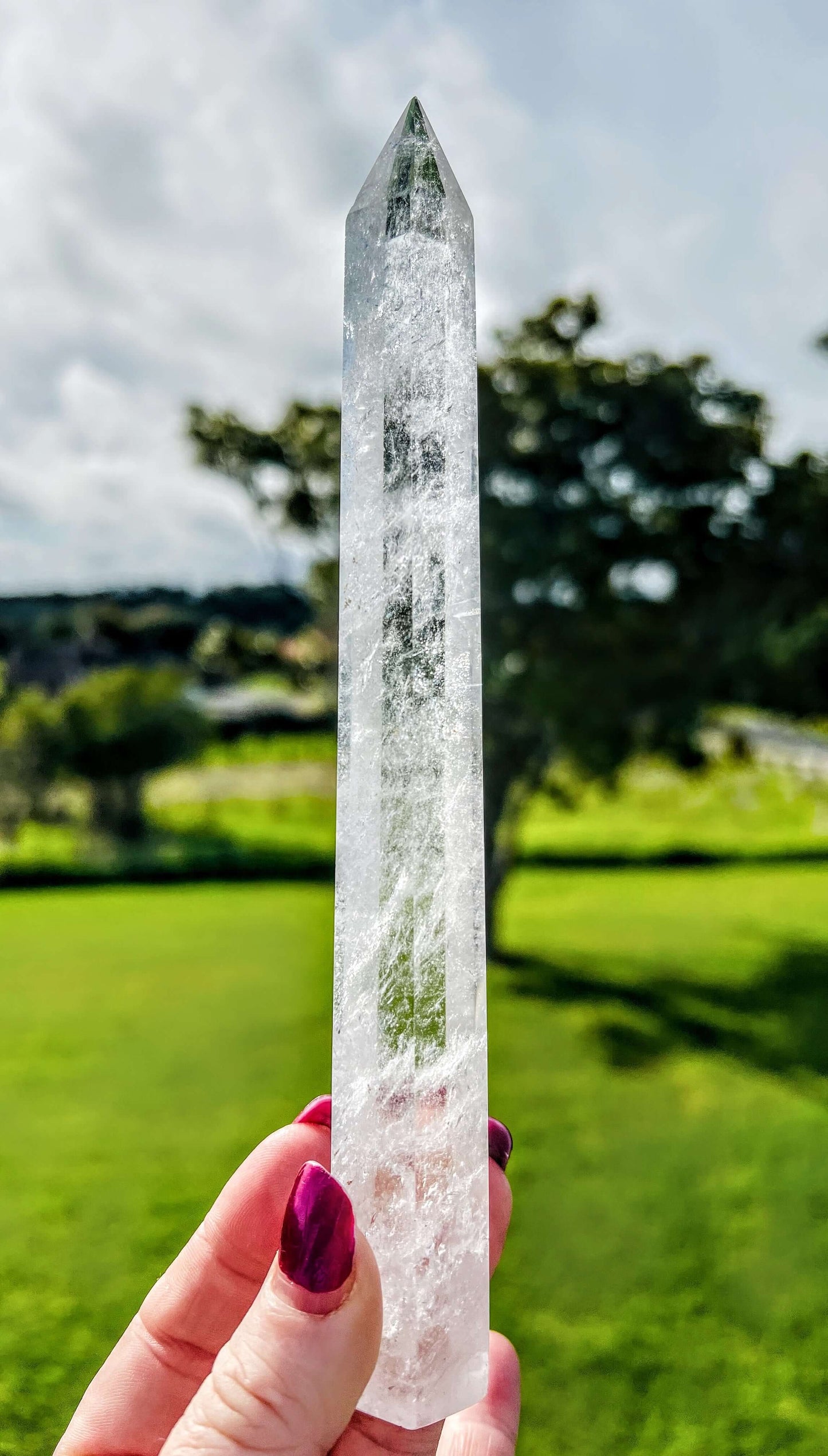 Clear quartz polished point held in hand with farm land in background.