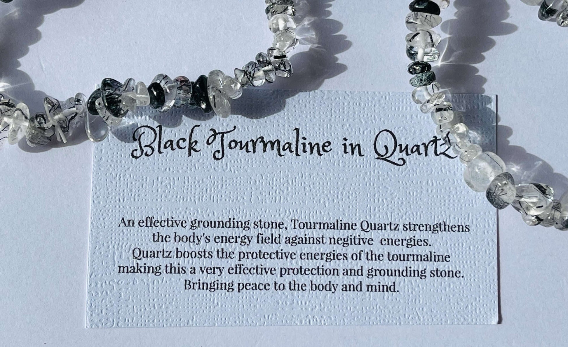 Black tourmaline in quartz crystal chip bracelet with information card on white background