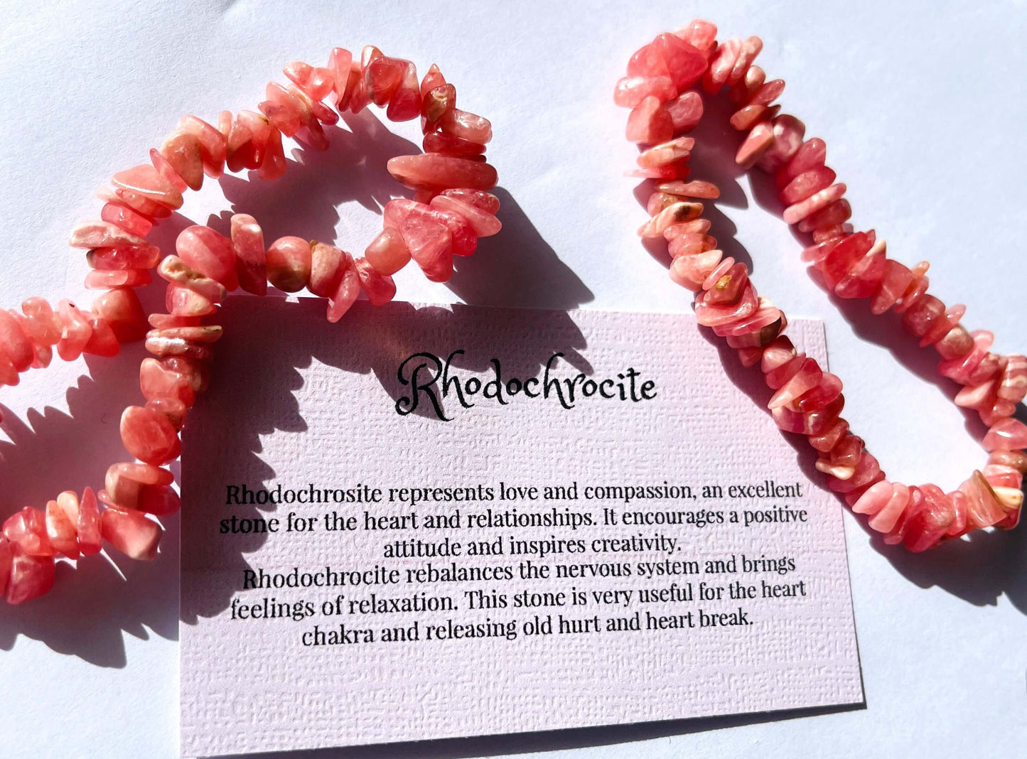 Rhodochrosite crystal chip bracelet with information card on white background