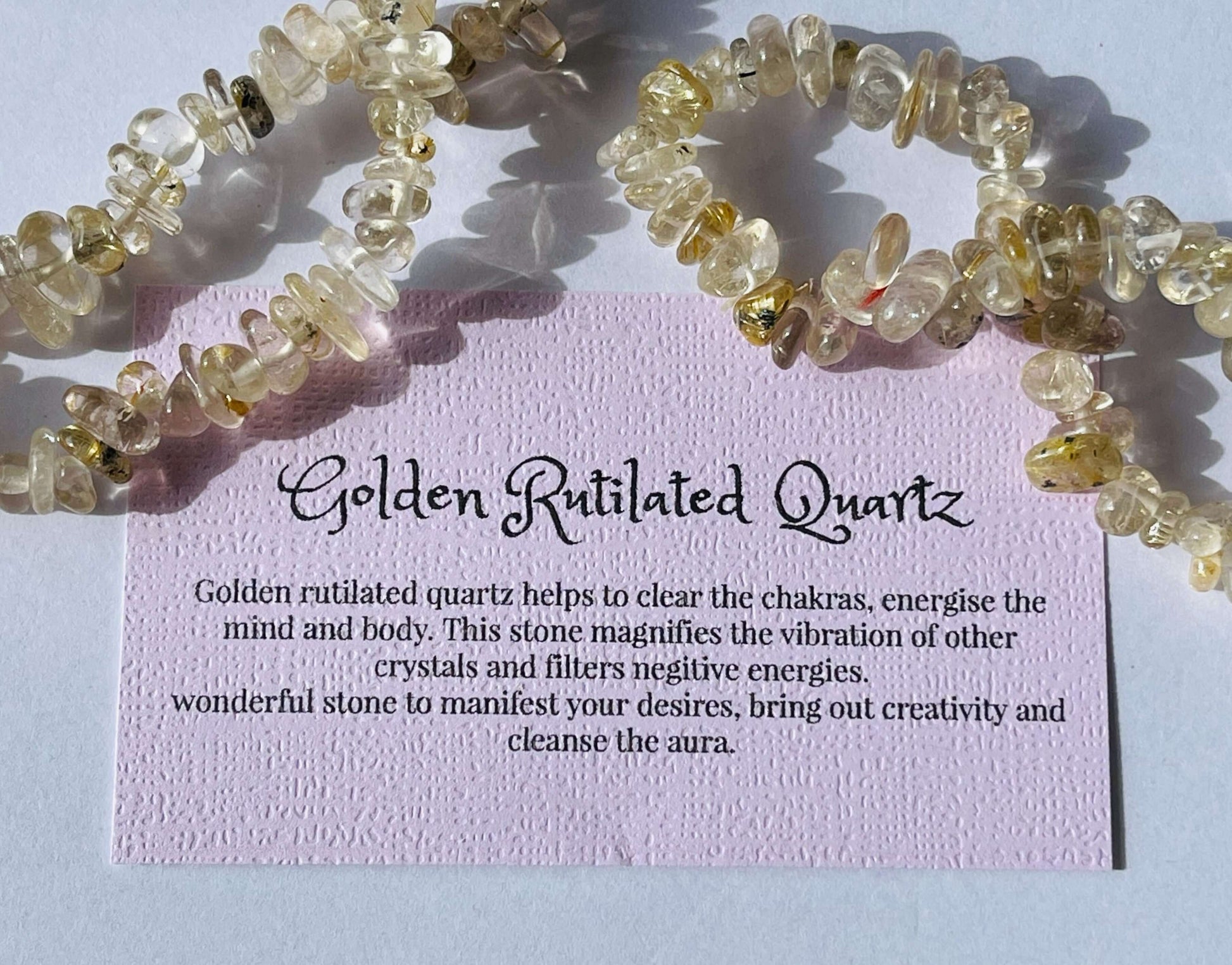 Golden rutilated quartz crystal chip bracelet with information card on white background