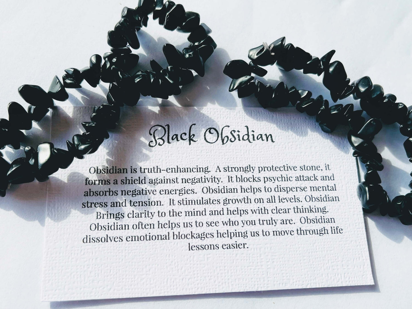 Black obsidian crystal chip bracelet with information card on white background