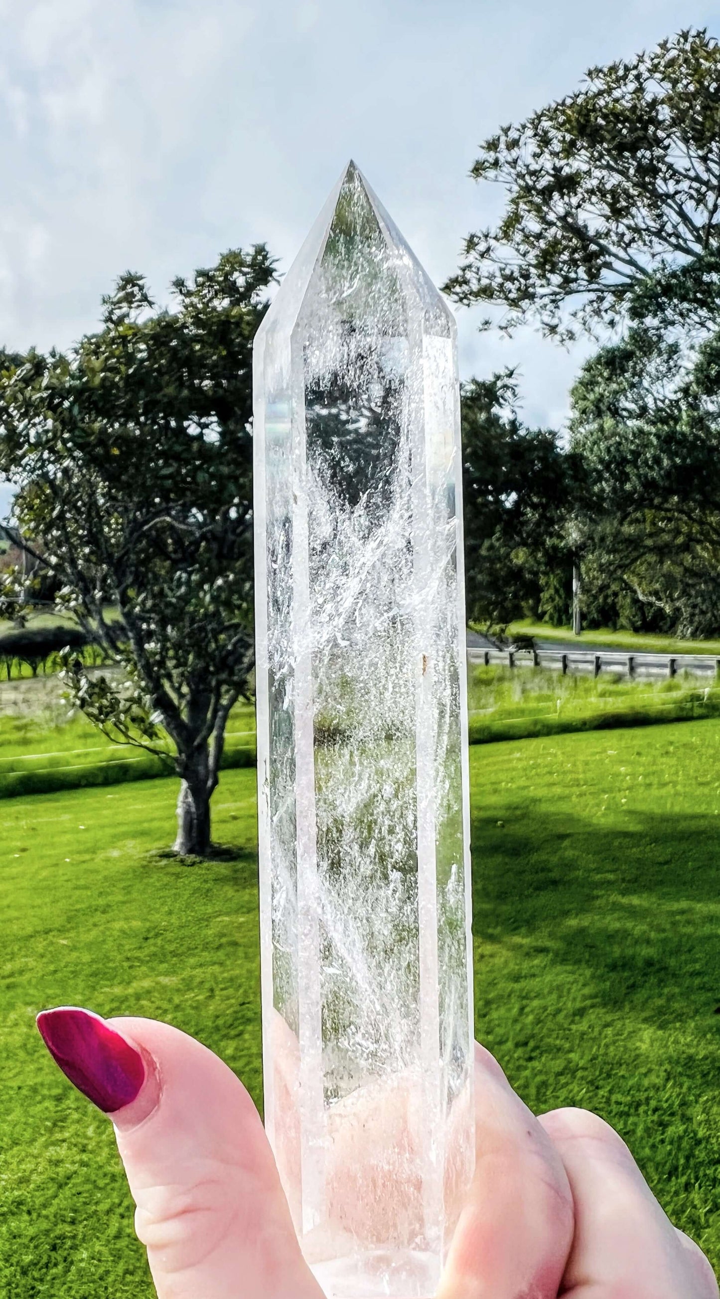 Clear quartz polished point held in hand with farm land in background.