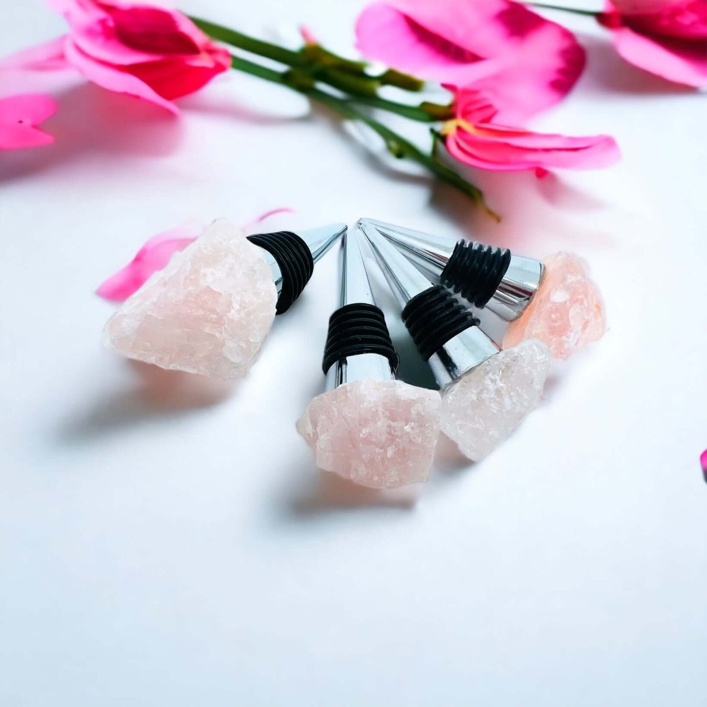 Rose quartz wine bottle stoppers on white surface with petals