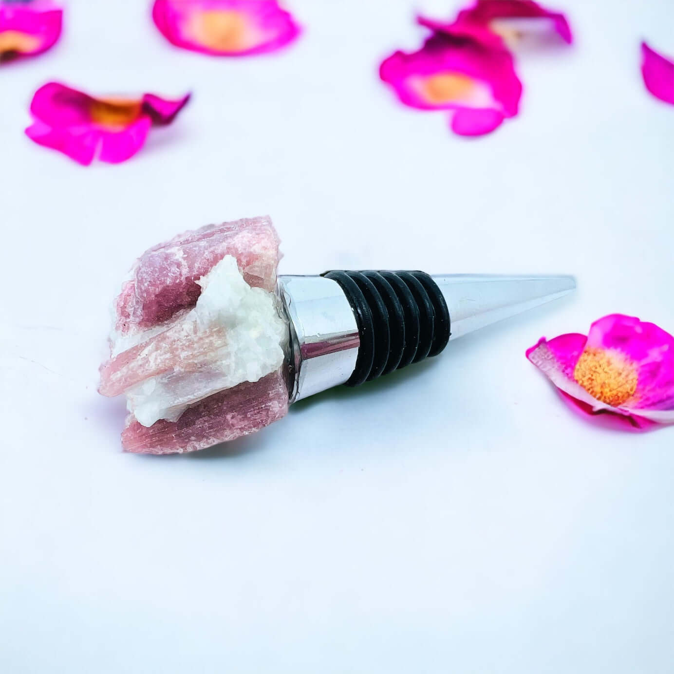 Pink tourmaline wine bottle stoppers on white surface with petals