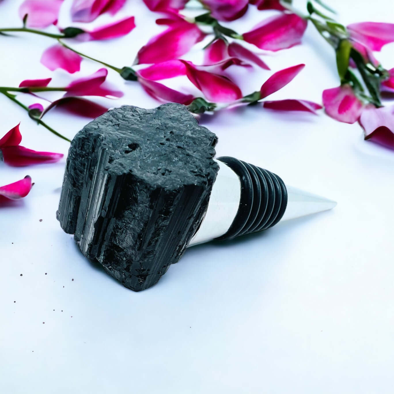 Black tourmaline wine bottle stoppers on white surface with petals