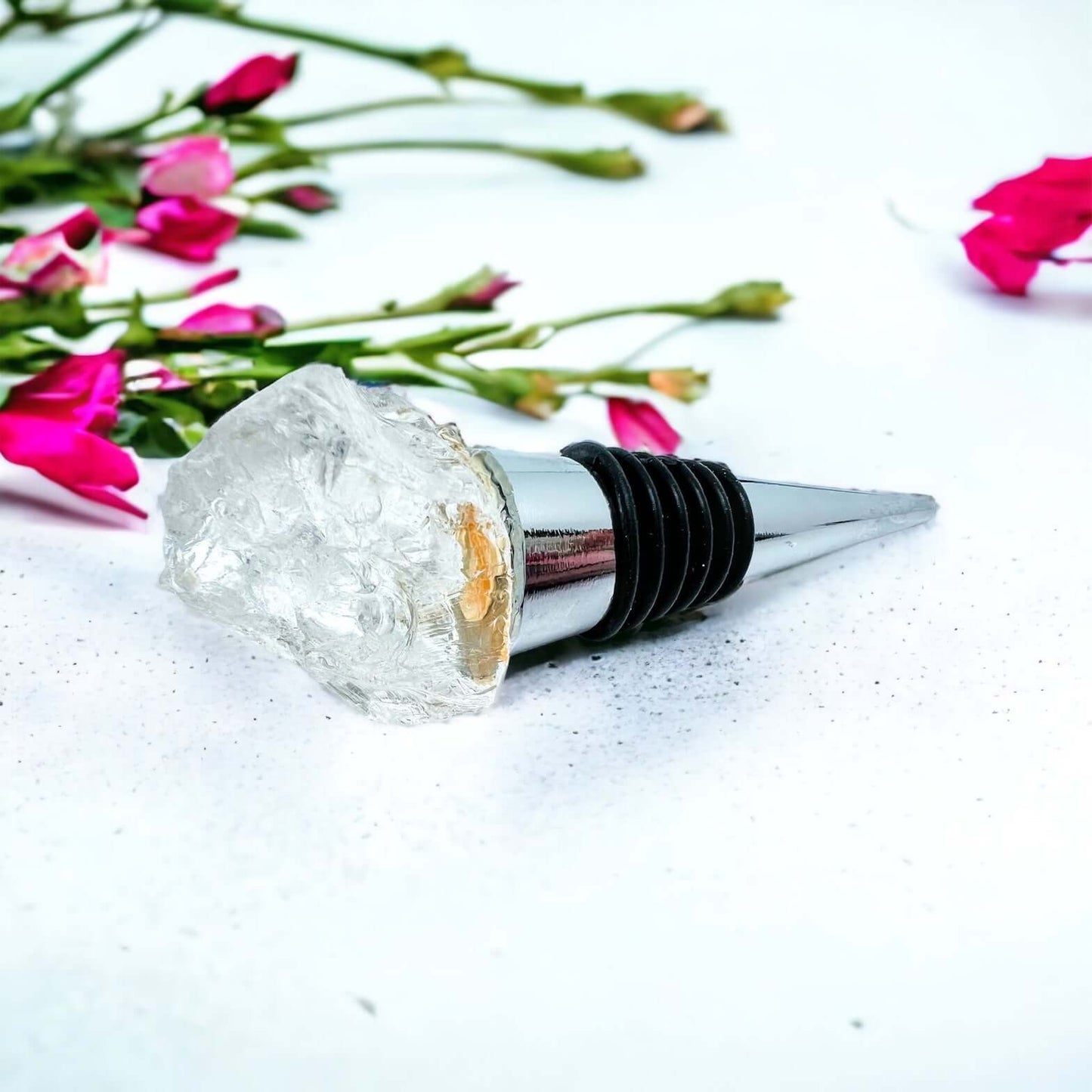 Clear quartz wine bottle stoppers on white surface with petals