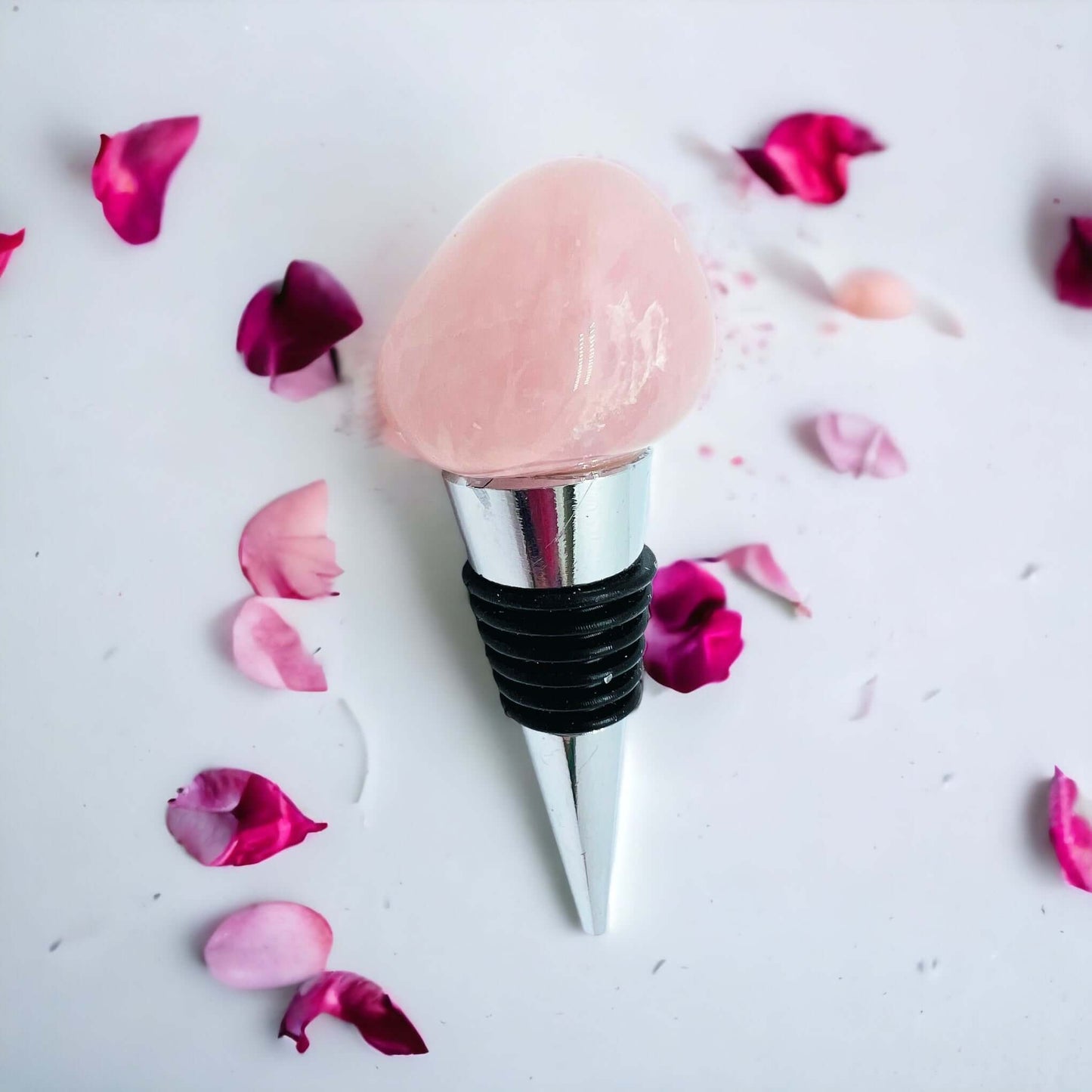 Rose quartz wine bottle stoppers on white surface with petals